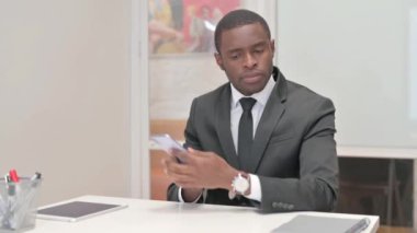 Afrikalı İşadamı bir bankta otururken telefonla konuşuyor.