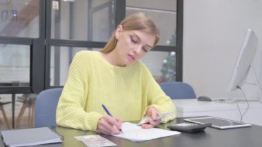 Genç sarışın kadın mali hesaplamalar yapıyor, para sayıyor.