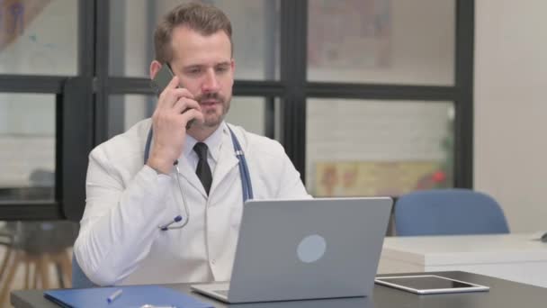 Μεσήλικας Γιατρός Μιλώντας Στο Τηλέφωνο Και Χρησιμοποιώντας Laptop — Αρχείο Βίντεο