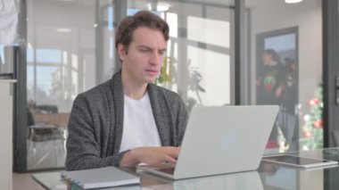 Ofisteki dizüstü bilgisayarda çalışırken kameraya bakan genç adam