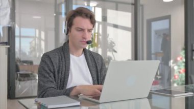Kulaklıklı genç adam Çağrı Merkezi 'nde laptopla çalışıyor.