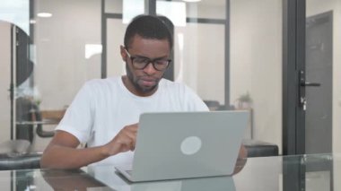 Ofiste dizüstü bilgisayarla çalışırken kameraya gülümseyen genç Afrikalı adam.