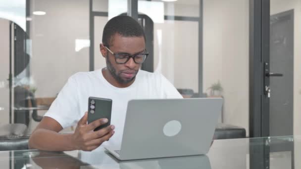 Mladý Afričan Pracující Notebooku Pomocí Chytrého Telefonu — Stock video