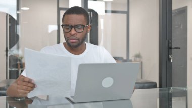 Young African Man Working on Documents and Laptop