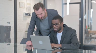 Orta yaşlı adam dizüstü bilgisayarda Afrikalı takım arkadaşına yardım ediyor.