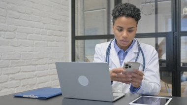 Klinikte telefon ve dizüstü bilgisayarla çalışan Afrikalı Kadın Doktor