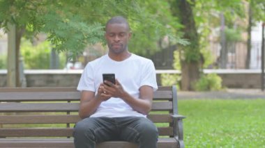 Park 'taki Bench' te oturan Afro-Amerikan Adam telefonda konuşuyor.