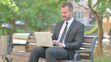 Genç İşadamı Dışarıda Dizüstü bilgisayar kullanırken Kameraya Gülümsüyor