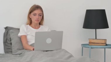Ciddi Genç Kadın Dizüstü bilgisayarla yataktayken Kameraya Bakıyor