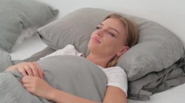 Yatakta yatarken kameraya bakan gülümseyen genç kadın.