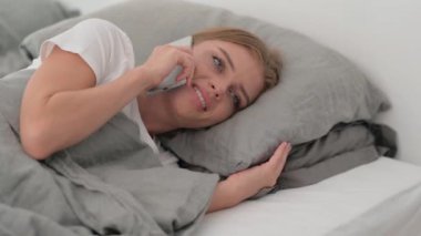 Yatakta yan yatarken telefonda konuşan genç kadın.