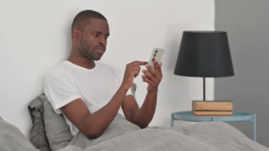 Afrikalı Adam Yatakta Otururken Akıllı Telefon Kullanıyor