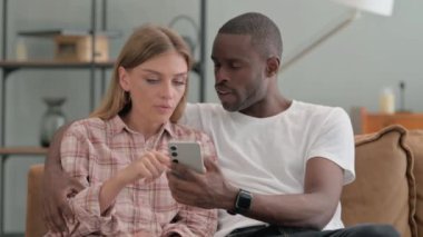 Evdeki koltukta otururken telefon kullanan ırklar arası bir çift.