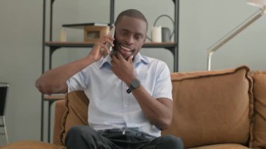 Evdeki koltukta oturan Afrikalı adam telefonda konuşuyor.