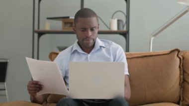Evdeki koltukta oturan Afrikalı adam evrak işleriyle uğraşıyor.