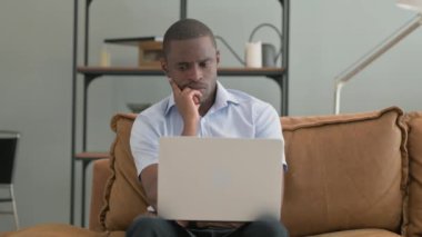 Kanepede otururken laptopta çalışan Dalgın Afrikalı Adam