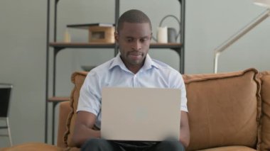 Kanepede otururken laptopta çalışan Dalgın Afrikalı Adam