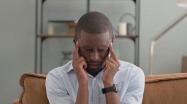 Evdeki koltukta oturan baş ağrısı olan Afrikalı adamın portresi.
