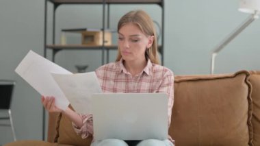 Evrak işleri yapan ve dizüstü bilgisayar kullanan genç bir kadın.