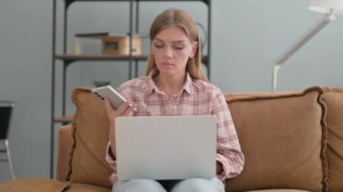 Genç kadın dışarıda dizüstü bilgisayar kullanırken telefonla konuşuyor.