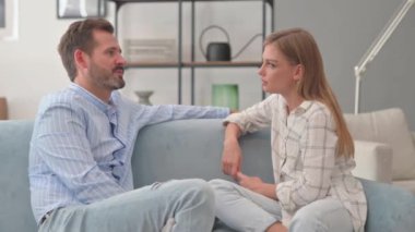 Evdeki koltukta oturan genç adam karısıyla konuşuyor.