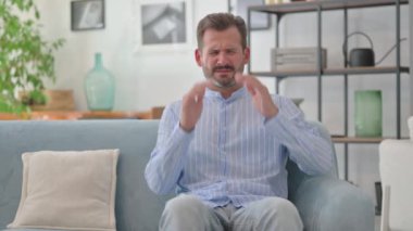 Orta yaşlı adam baş ağrısı çekiyor. Evdeki koltukta oturuyor.