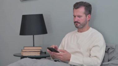 Kızgın Orta yaşlı adam yatakta telefonla konuşuyor.