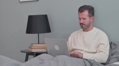 Baş ağrısı olan orta yaşlı bir adam laptopta çalışıyor.