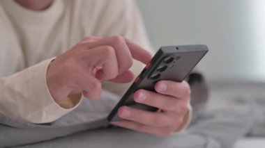 Erkek El, yatakta karın üstü yatarken telefonu kullanıyor.