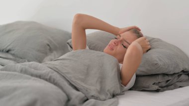 Yatakta uyurken migren ağrısı çeken genç bir kadın.