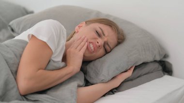 Dişleri ağrıyan genç bir kadın yatakta yatıyor.