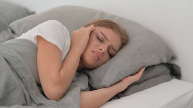 Yatakta yatarken migren ağrısı çeken genç bir kadın.