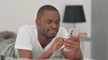 Afrikalı Adam Yatakta Mide Uzanırken Telefonu Kullanıyor