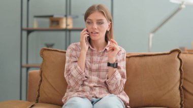 Evdeki kanepede oturan genç bir kadın telefonda konuşuyor.