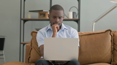 Kanepede otururken laptopta çalışan Dalgın Afrikalı Adam