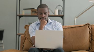 Kanepede otururken laptopta çalışan Dalgın Afrikalı Adam