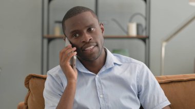 Evdeki koltukta oturan Afrikalı adam telefonda konuşuyor.