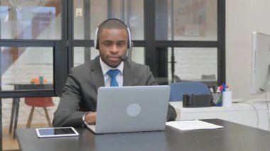 Kulaklıklı Afrikalı Amerikalı İşadamı Bilgisayarda çalışırken Kameraya Bakıyor