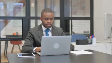 Dizüstü bilgisayar üzerinde çalışırken kameraya bakan Afrikalı Amerikalı İşadamı