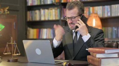 Öfkeli Orta Çağ Avukatı Laptop kullanırken telefonla konuşuyor