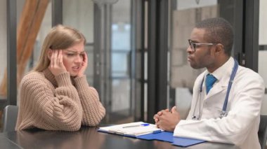 Baş ağrısı olan kadın hasta Afrikalı erkek doktorla konuşuyor.
