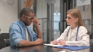 Baş ağrısı olan Afrikalı bir adam kadın doktorla konuşuyor.