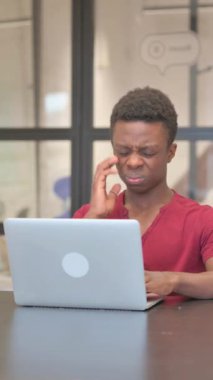 Genç Afrikalı adamın dizüstü bilgisayarda yazarken baş ağrısı çektiği dikey video