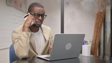 Bilgisayarda çalışırken telefonda konuşan Afrikalı Adam