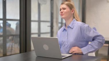 Sırt ağrısı olan genç bir kadın dizüstü bilgisayarda çalışıyor.