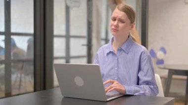 Boyun ağrısı olan genç bir kadın dizüstü bilgisayarda çalışıyor.