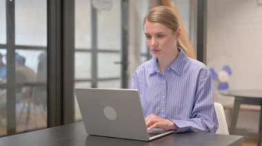 Baş ağrısı olan genç bir kadın dizüstü bilgisayarda çalışıyor.