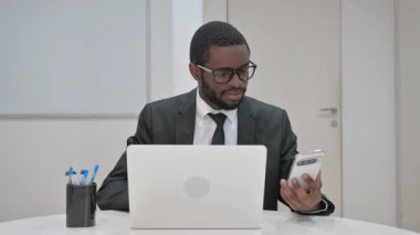 dizüstü bilgisayarda çalışırken akıllı telefon kullanan işadamı