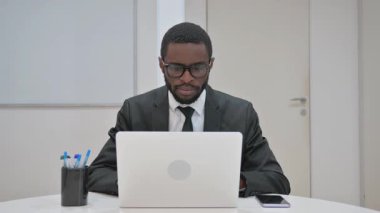 Afrika kökenli Amerikalı iş adamı ofisteyken kameraya bakıyor.