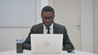 Onaylamayan Afrikalı Amerikalı işadamı, ofis masasından memnuniyetsizliğini ileterek baş parmağıyla bir jest yapıyor.